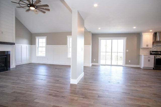 unfurnished living room featuring ceiling fan, a large fireplace, a wainscoted wall, dark wood-style flooring, and recessed lighting