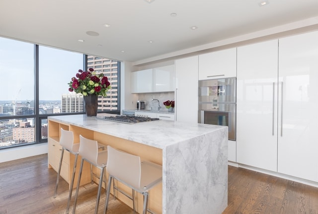 kitchen with light stone counters, dark wood-type flooring, white cabinetry, stainless steel appliances, and a breakfast bar