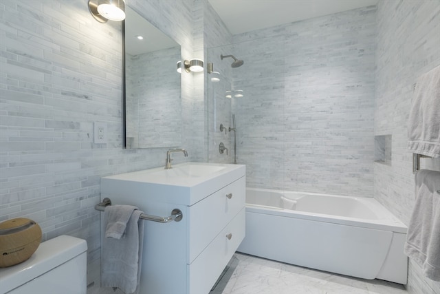 full bathroom with tile walls, tiled shower / bath, vanity, and toilet