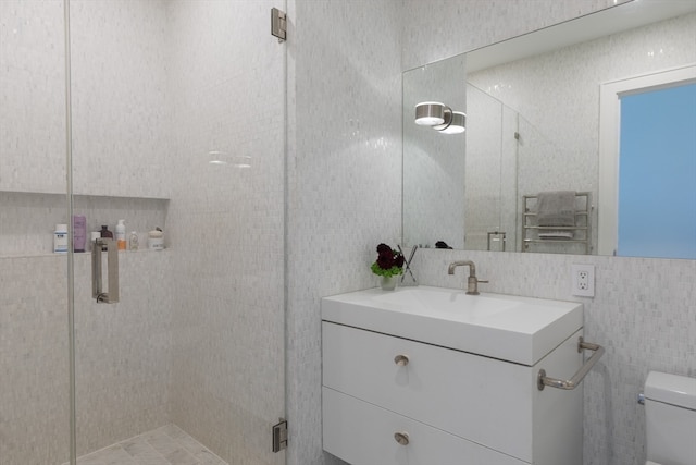 bathroom with tile walls, a shower with shower door, vanity, and toilet