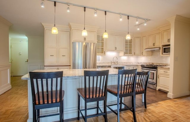 111 Perkins St Unit 42, Boston, MA 02130 - kitchen featuring appliances with stainless steel finishes, under cabinet range hood, tasteful backsplash, a center island, and wainscoting