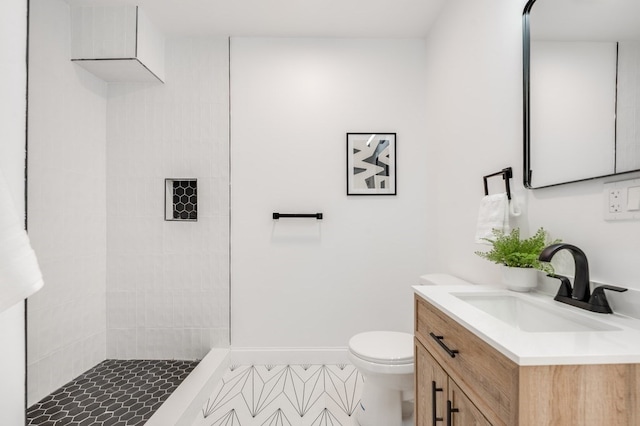 bathroom with tile patterned flooring, vanity, tiled shower, and toilet