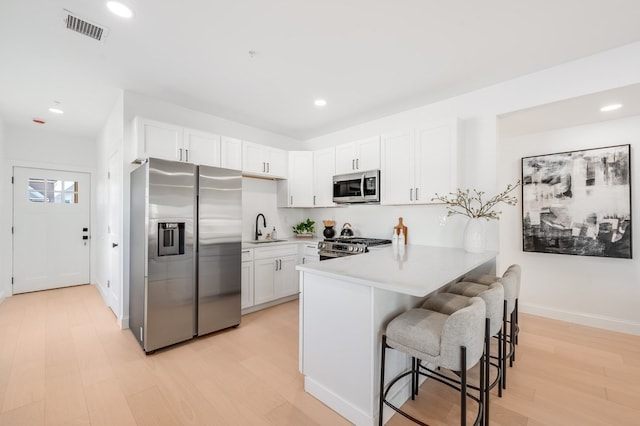 kitchen with kitchen peninsula, stainless steel appliances, sink, white cabinetry, and a breakfast bar area