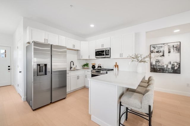 kitchen with sink, light wood-type flooring, white cabinetry, kitchen peninsula, and stainless steel appliances