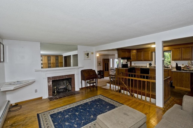 118 Woodland Rd, Springfield, MA 01129 - living room with wood finished floors, a baseboard heating unit, a textured ceiling, a fireplace, and healthy amount of natural light