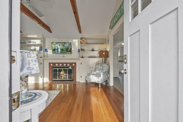 foyer entrance featuring a ceiling fan, wood finished floors, beamed ceiling, and a fireplace
