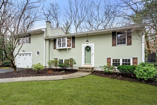 raised ranch featuring a garage, a chimney, a front yard, and aphalt driveway
