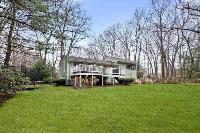 rear view of house with a lawn, a wooden deck, fence, and a trampoline