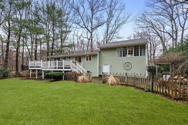 rear view of house featuring roof with shingles, fence, a wooden deck, a lawn, and stairway