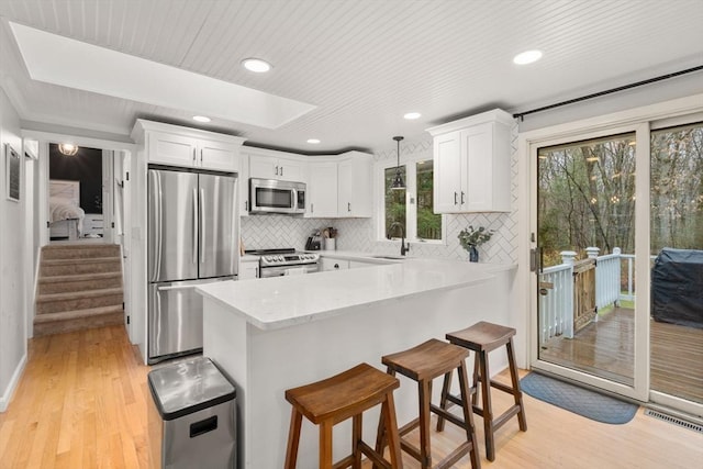 kitchen featuring stainless steel appliances, a sink, light wood-type flooring, white cabinetry, and a breakfast bar area