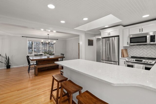 kitchen with stainless steel appliances, light wood-type flooring, light stone countertops, decorative backsplash, and white cabinetry