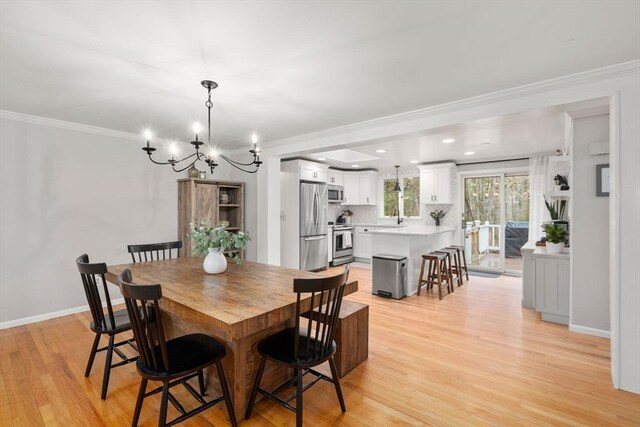 dining room featuring light wood-type flooring, baseboards, ornamental molding, and an inviting chandelier