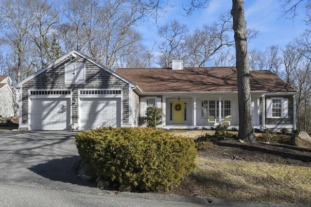 view of front facade featuring a garage, a chimney, a porch, and driveway