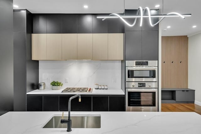 kitchen with a sink, stainless steel appliances, modern cabinets, dark cabinetry, and light stone countertops