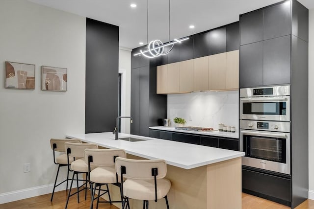 kitchen featuring appliances with stainless steel finishes, dark cabinets, a breakfast bar area, light wood finished floors, and recessed lighting