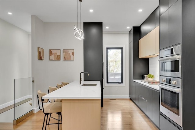kitchen featuring a sink, light wood-type flooring, a breakfast bar area, hanging light fixtures, and a kitchen island with sink