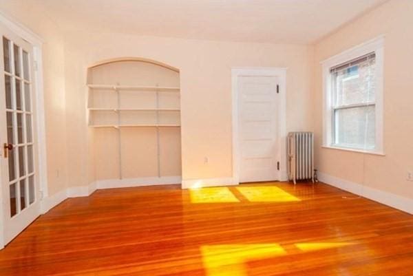 unfurnished room with radiator heating unit, wood finished floors, and baseboards