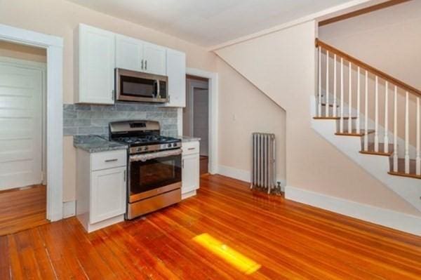 kitchen with radiator, wood finished floors, white cabinets, appliances with stainless steel finishes, and backsplash