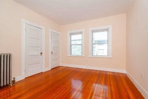 unfurnished room featuring baseboards, wood finished floors, and radiator heating unit