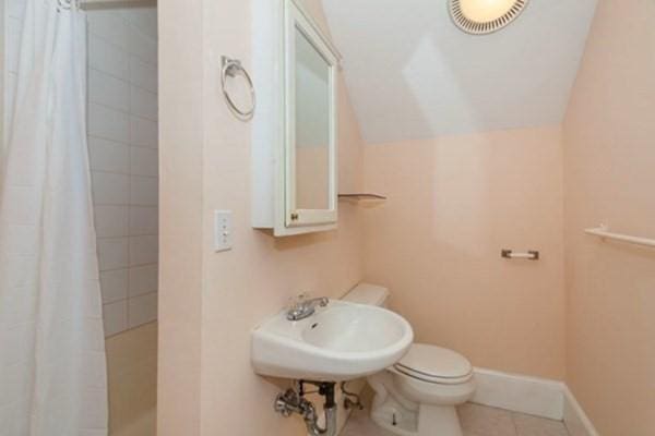 full bath with tile patterned flooring, baseboards, toilet, a tile shower, and a sink