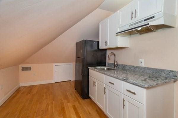 kitchen featuring light stone countertops, a sink, light wood-style floors, under cabinet range hood, and white cabinetry