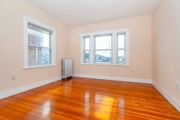 empty room featuring baseboards, a healthy amount of sunlight, wood finished floors, and radiator heating unit