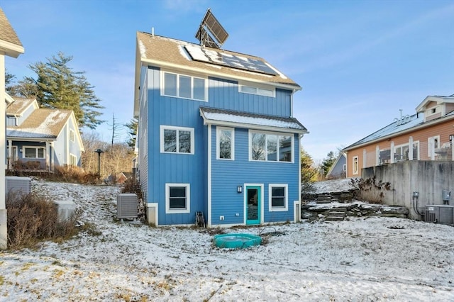 snow covered house featuring solar panels and central AC