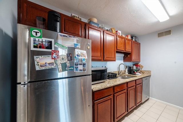 kitchen with sink, stainless steel appliances, light stone counters, a textured ceiling, and light tile patterned floors