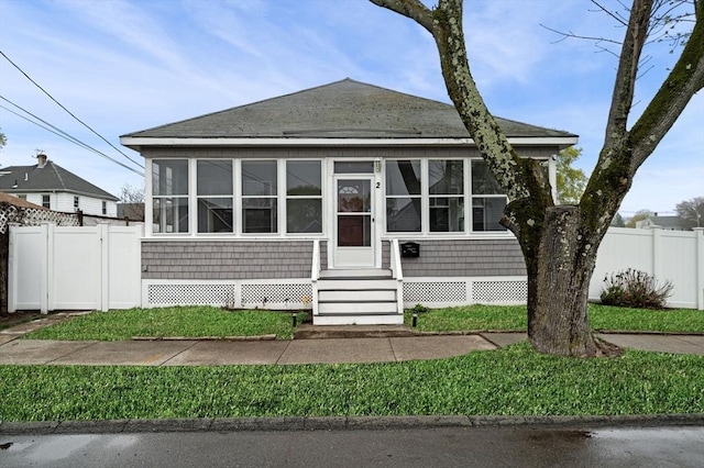 bungalow-style home featuring a sunroom, fence, and roof with shingles