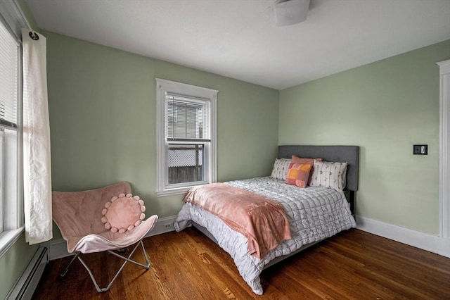 bedroom with wood finished floors, a baseboard heating unit, and baseboards