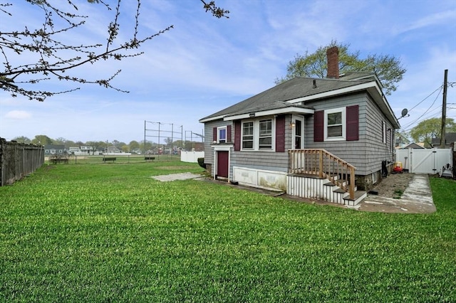 rear view of house featuring a gate, fence, a chimney, and a yard