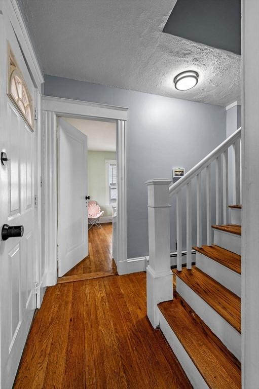 foyer with a baseboard heating unit, stairway, baseboards, a textured ceiling, and wood finished floors