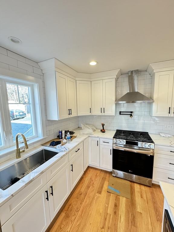 kitchen with a sink, stainless steel range with gas cooktop, decorative backsplash, wall chimney exhaust hood, and light wood finished floors