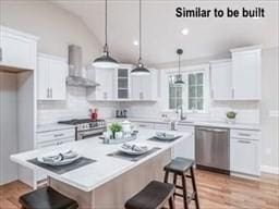 kitchen with wall chimney exhaust hood, light countertops, appliances with stainless steel finishes, white cabinetry, and a kitchen breakfast bar