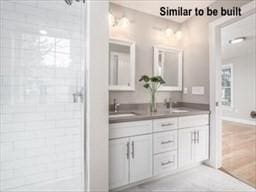 full bath featuring double vanity, a sink, and tiled shower