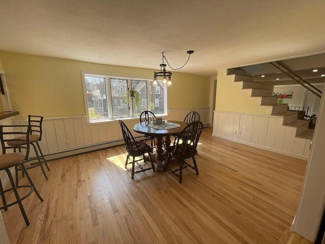 dining area with wood finished floors, stairway, a baseboard heating unit, a chandelier, and a wainscoted wall