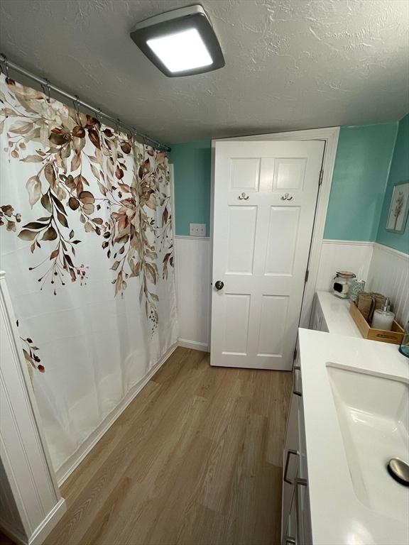 bathroom with a textured ceiling, wainscoting, and wood finished floors