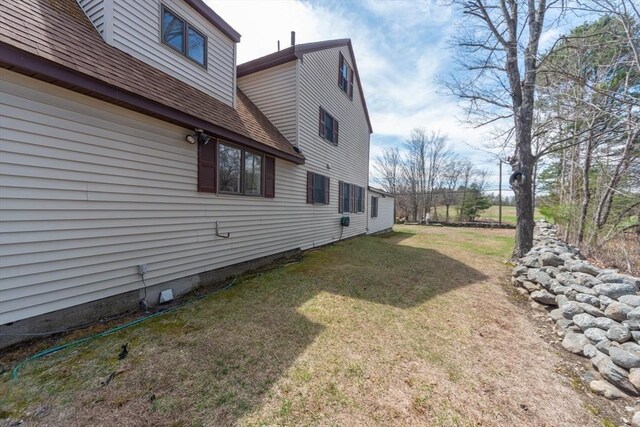 view of side of home featuring a shingled roof and a yard