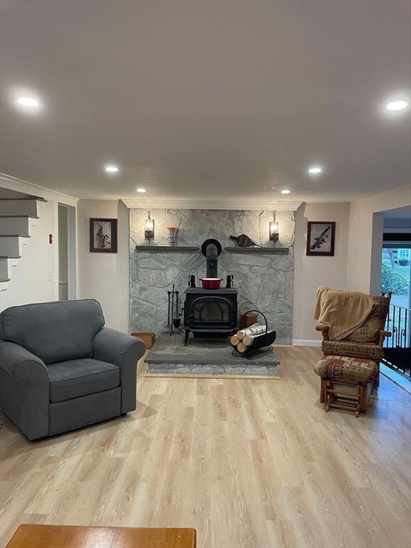 living area with a wood stove, recessed lighting, wood finished floors, and stairway