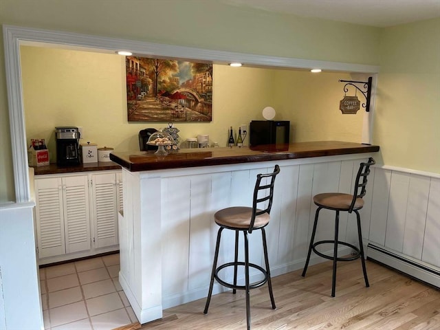 bar featuring wainscoting, light wood-style floors, a baseboard radiator, refrigerator, and bar area