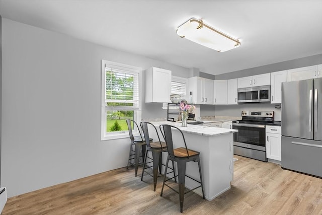 78 Conserve Ave, Westport, MA 02790 - kitchen featuring appliances with stainless steel finishes, a peninsula, white cabinetry, a breakfast bar, and light wood finished floors