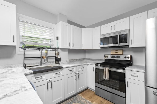 78 Conserve Ave, Westport, MA 02790 - kitchen featuring appliances with stainless steel finishes, a sink, white cabinets, light wood-style flooring, and light stone countertops