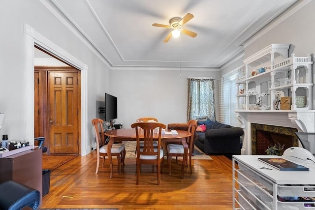dining area featuring crown molding, a ceiling fan, wood finished floors, and a fireplace