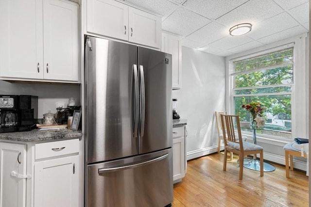 kitchen with freestanding refrigerator, a drop ceiling, light wood-type flooring, dark stone counters, and white cabinetry