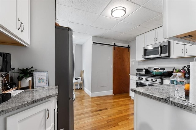 kitchen featuring a barn door, white cabinets, stone counters, stainless steel appliances, and light wood-style flooring