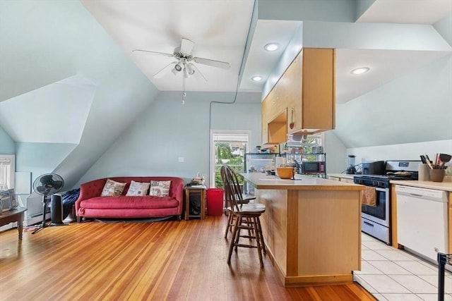 kitchen featuring a breakfast bar area, a ceiling fan, white dishwasher, vaulted ceiling, and gas stove