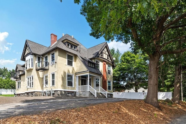 victorian house featuring stucco siding, a shingled roof, fence, and a chimney
