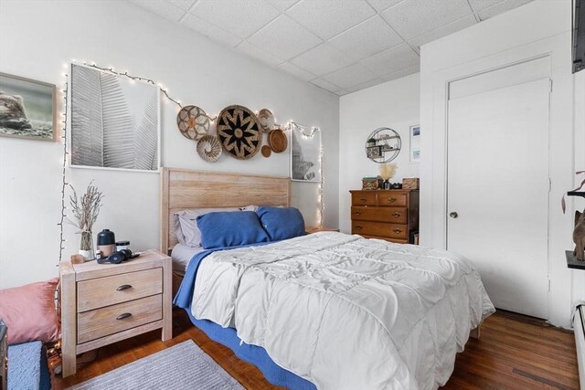 bedroom with a paneled ceiling, baseboard heating, and wood finished floors