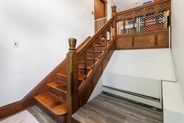 stairs featuring a baseboard heating unit and wood finished floors