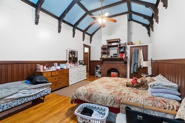 bedroom with high vaulted ceiling, wood walls, wainscoting, and a fireplace
